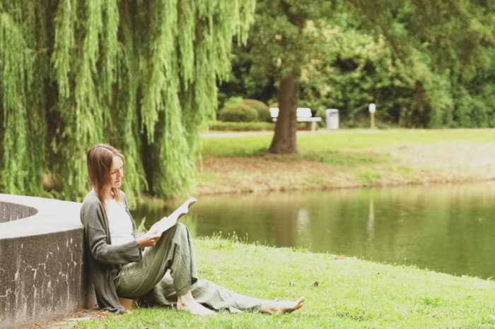 Tatjana an einem Teich sitzend und ein Buch über Yoga lesend